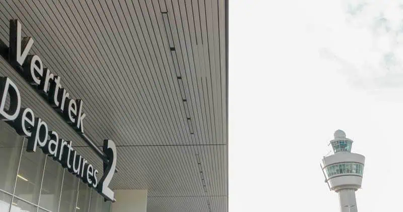Vertrekhal van Schiphol met vertrekborden en controletoren.